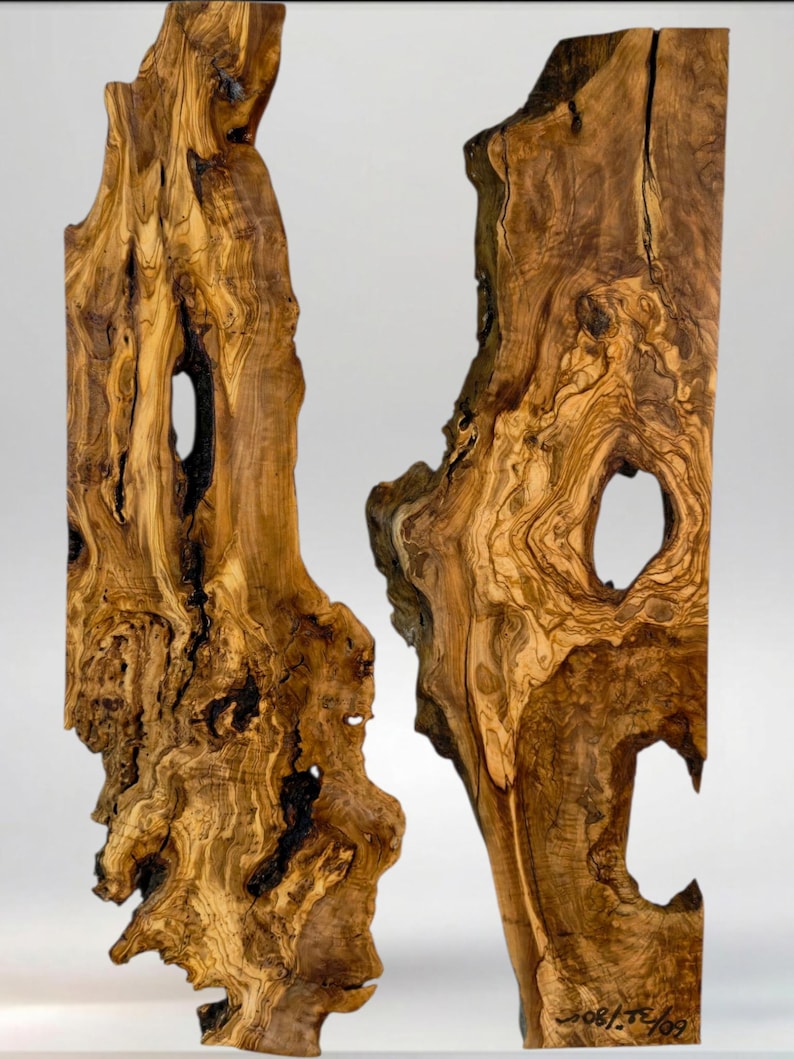 May include: Two vertical, irregular-shaped wooden sculptures with a natural, organic aesthetic. The wood grain is prominent, with swirling patterns in shades of brown and tan. Each piece has a large, irregular hole. The overall effect is rustic and artistic.