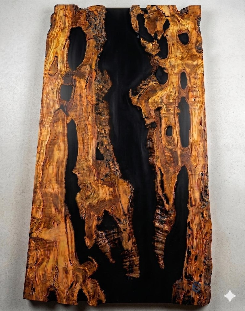 May include: A large, rectangular wooden slab with a striking design. The wood features a natural, warm brown color with intricate grain patterns and dark, irregular voids. A central, glossy black resin fills the gaps, creating a dramatic contrast.