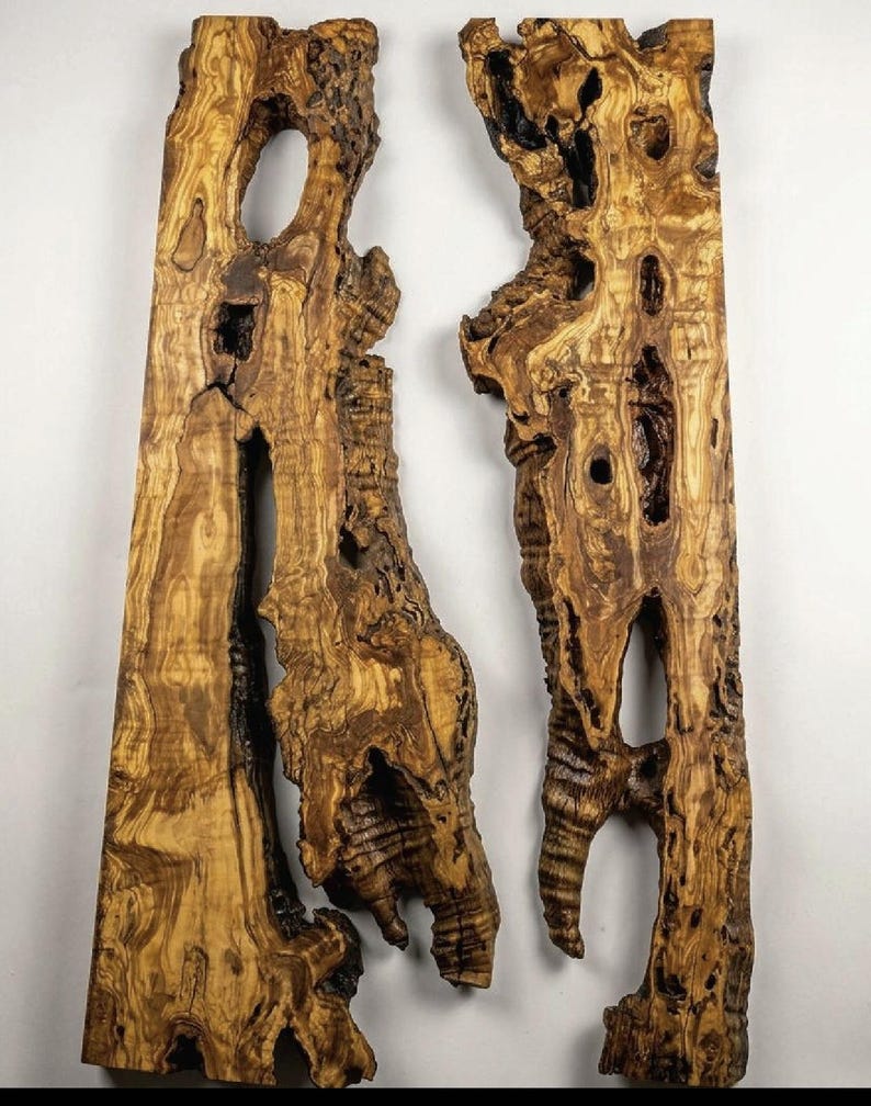 May include: Two irregularly shaped wooden planks with a natural, textured appearance. The planks are primarily brown with darker streaks and knots, featuring several holes and organic edges. The wood grain is visible, creating a rustic aesthetic.