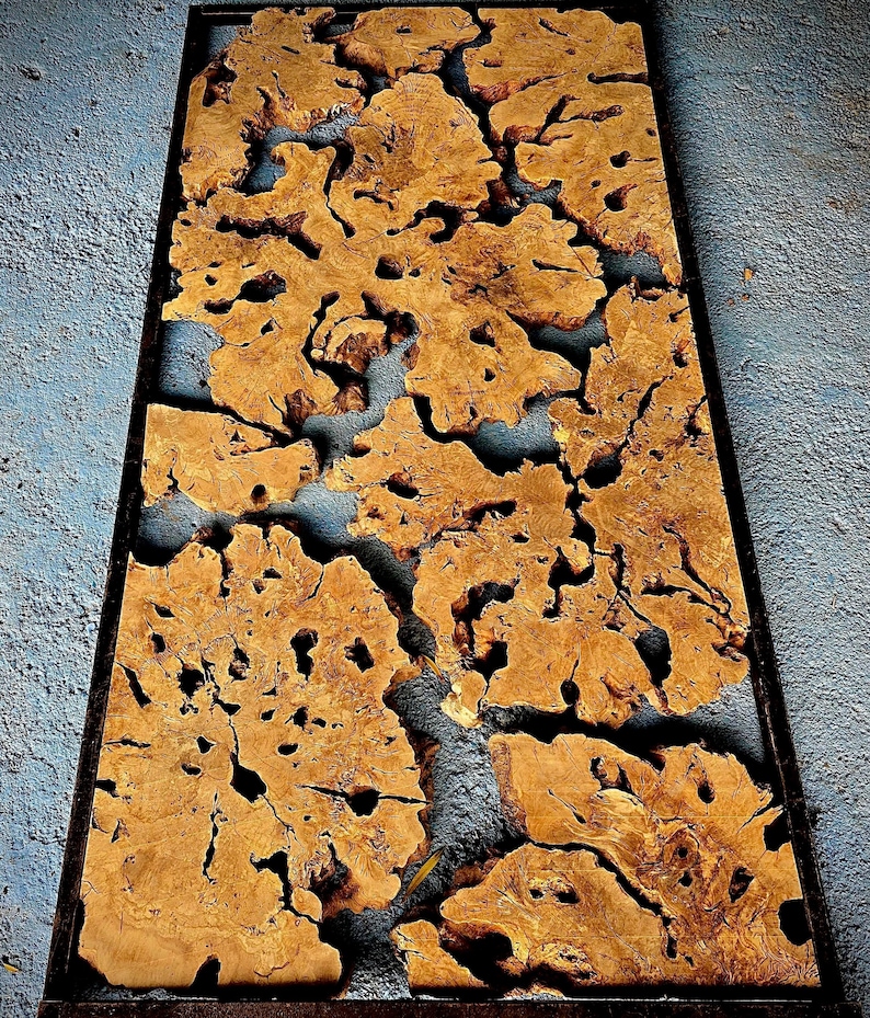 May include: A large piece of wood with a unique, intricate pattern of knots and burls. The wood is a light brown color and has been polished to a smooth finish. The wood is framed in a black metal frame.