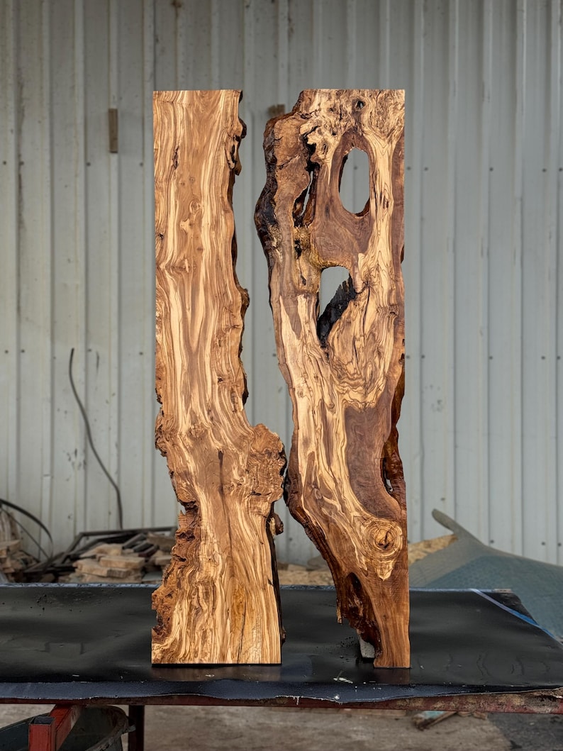 May include: Two vertical, raw-edge wooden slabs with a natural, organic aesthetic. The wood grain is prominent, showcasing a mix of light and dark brown tones. One slab has a large, irregular hole. The slabs are displayed against a neutral background.