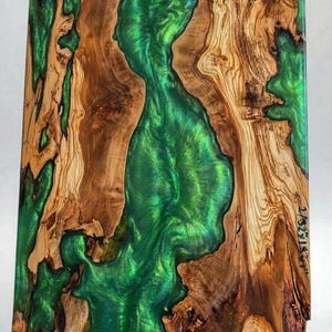 May include: A rectangular wooden art piece with a vibrant green epoxy river flowing through the center. The wood has a natural, light brown grain pattern. The epoxy river has a glossy, reflective surface.