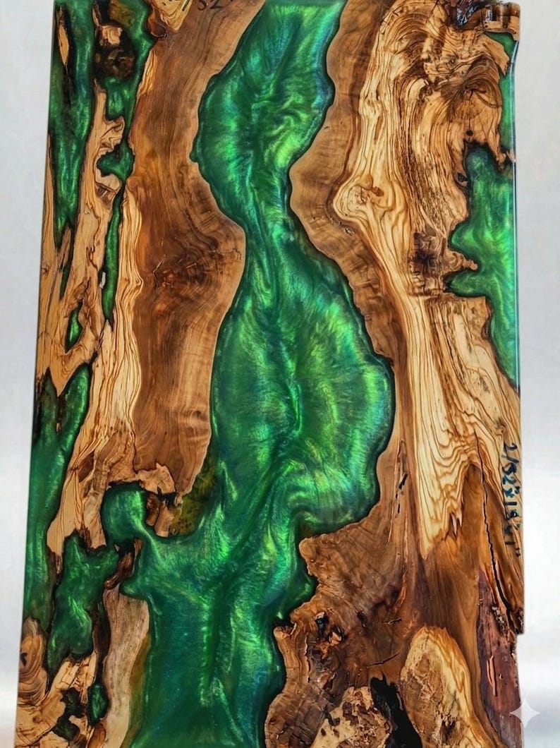 May include: A rectangular wooden art piece with a vibrant green epoxy river flowing through the center. The wood has a natural, light brown grain pattern. The epoxy river has a glossy, reflective surface.