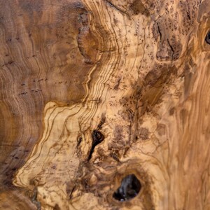 May include: A polished wooden surface featuring a complex, swirling grain pattern in shades of light tan, golden yellow, and deep brown. The texture displays natural knots, organic dark streaks, and intricate burl wood formations throughout.