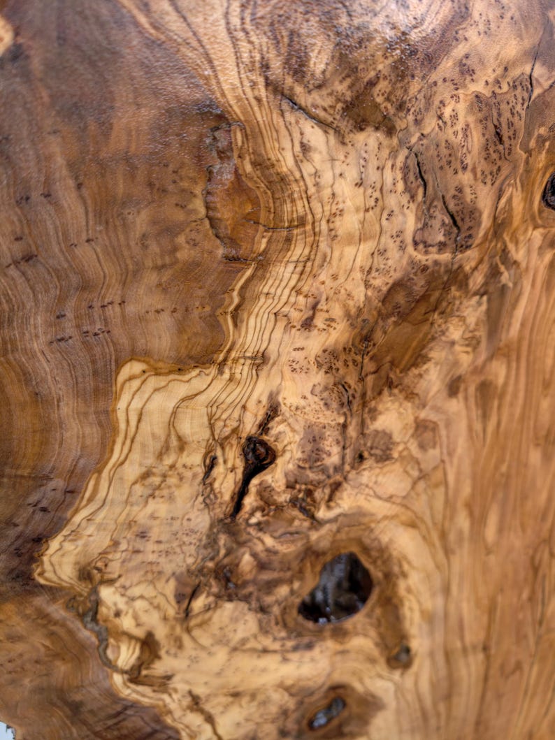 May include: A polished wooden surface featuring a complex, swirling grain pattern in shades of light tan, golden yellow, and deep brown. The texture displays natural knots, organic dark streaks, and intricate burl wood formations throughout.