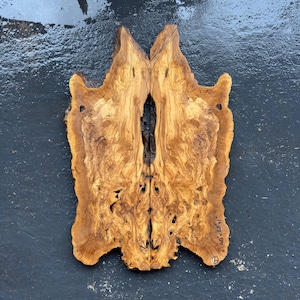 Könnte beinhalten: Zwei passende, unregelmäßig geformte Holzplatten mit einem natürlichen, hellbraunen Maserungsmuster. Die Platten sind in der Mitte verbunden und bilden ein symmetrisches Design. Das Holz hat eine raue Textur mit einigen Löchern und Unvollkommenheiten. Maße: 40 x 35 x 07 cm.