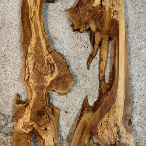 May include: Two irregularly shaped, unfinished wooden slabs with natural edges. The wood grain features a mix of light and dark brown tones, with visible knots and unique patterns. The slabs are likely for woodworking projects.