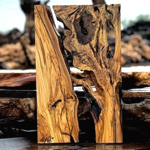 May include: A rectangular, handcrafted wooden art piece with a natural, organic aesthetic. The wood features a mix of light and dark brown tones, with intricate grain patterns and a split down the center. The text "10/16" is visible on the lower left corner.