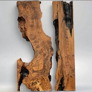 May include: Two irregularly shaped wooden slabs with a natural, rustic appearance. The wood features a mix of light and dark brown tones, with areas of black charring. The text "3/16" is visible on one slab. The slabs have a raw, unfinished look.