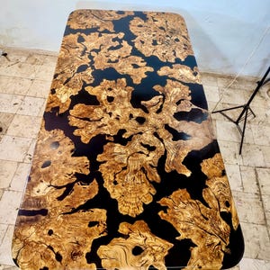 May include: A rectangular table top with a black epoxy resin finish and a natural wood inlay. The wood has a unique pattern of knots and swirls, creating a rustic and organic look.
