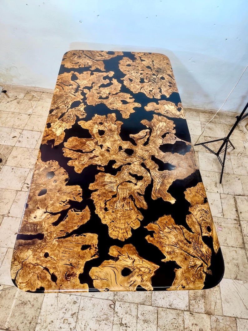 May include: A rectangular table top with a black epoxy resin finish and a natural wood inlay. The wood has a unique pattern of knots and swirls, creating a rustic and organic look.