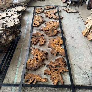 May include: A collection of wood slices with intricate grain patterns are arranged in a metal frame. The wood is a light brown color with dark brown streaks. The frame is black and has a simple design.