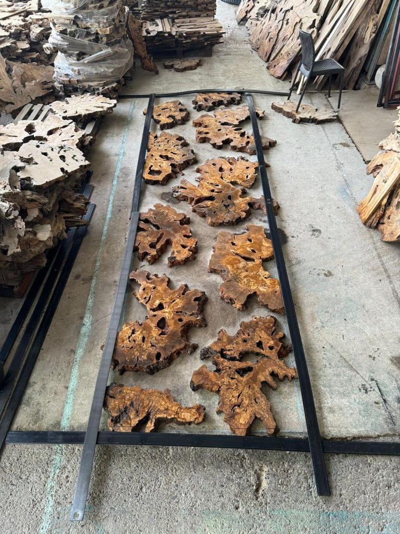 May include: A collection of wood slices with intricate grain patterns are arranged in a metal frame. The wood is a light brown color with dark brown streaks. The frame is black and has a simple design.