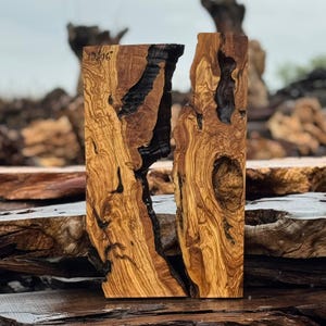 May include: Two rectangular wooden blocks with a natural wood grain pattern. The wood is a mix of light and dark brown, with black accents in the center. The blocks have a rough, textured surface and are standing upright.