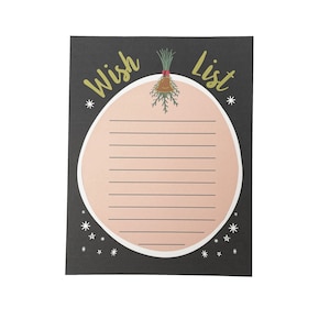 May include: A black notepad with the words "Wish List" in gold script. The notepad features a pink circle with lines for writing, and decorative stars. A festive bell and greenery design is above the circle.