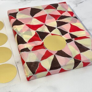 a flat lay view of a 2-inch round matte gold sticker shown in use on a package wrapped in tissue paper with 4 unused stickers set beside the package for perspective