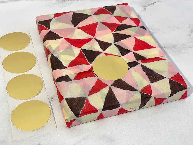 a flat lay view of a 2-inch round matte gold sticker shown in use on a package wrapped in tissue paper with 4 unused stickers set beside the package for perspective