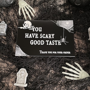 May include: Black and white thank you card with a spider web, spider, and moon with a skull. The text reads "You have scary good taste. Thank you for your order."