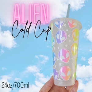 May include: A clear cold cup with a lid and straw, decorated with a pattern of colourful alien faces. The cup holds 700ml. The words "ALIEN Cold Cup" are displayed in pink neon against a blue sky background.