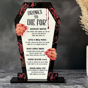 May include: A black coffin-shaped sign with the text "DRINKS TO DIE FOR" in white. The sign features a list of Halloween-themed cocktails, with red accents and illustrations of hands with long, red nails.