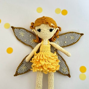 May include: A handmade crochet doll featuring golden-yellow hair, a cream-colored body, and a layered yellow skirt. The doll has large black bead eyes and expansive grey wings decorated with embroidered yellow star patterns and golden-yellow edges.