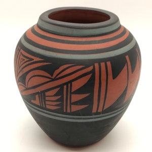 May include: A small, round, black and red pottery vase with geometric designs. The vase has a black base and a red band with black geometric designs.