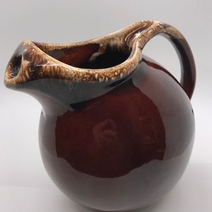 May include: A brown ceramic jug with a white rim and a brown handle. The jug has a round body and a wide mouth.
