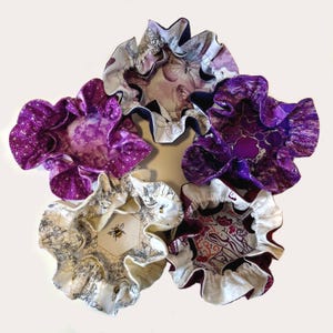 May include: Five fabric bowls with ruffled edges. The bowls are in various patterns, including purple, white, and black. The bowls are perfect for holding small items like jewelry or trinkets.