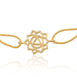 Può includere: Un braccialetto chakra dorato con un design delicato e intricato. Il braccialetto è realizzato con un cordoncino sottile e intrecciato e presenta un ciondolo a forma di chakra Anahata, il chakra del cuore.