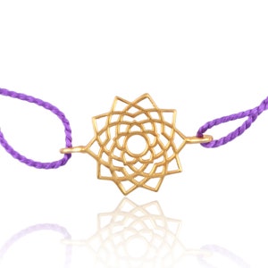 May include: A gold-colored chakra charm with a delicate, intricate design, attached to a purple cord bracelet.