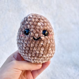 May include: A brown crocheted plush toy shaped like a potato with a smiling face and black eyes.