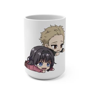 May include: White ceramic mug featuring a cartoon illustration of two anime-style characters. One character has black hair and a pink outfit, the other has blonde hair and a black outfit. The characters are drawn in a chibi style.