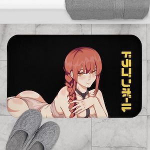 May include: Black bath mat featuring an anime-style illustration of a person with red hair and a black background. The mat has Japanese text in yellow on the right side. Gray slippers are in the foreground.