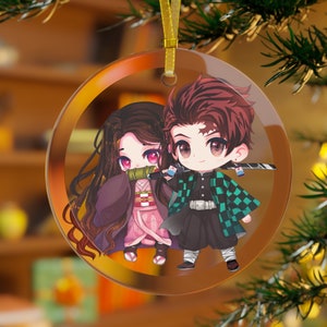 May include: A clear, round Christmas ornament featuring a cartoon illustration of two anime characters. The characters are a male and female, with the male holding a sword. The ornament has a gold ribbon for hanging.