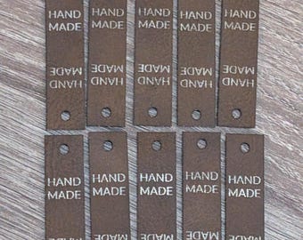 May include: A collection of brown rectangular tags with the words "HAND MADE" printed in white. Each tag has a small hole at the top and bottom. The tags are arranged in rows.