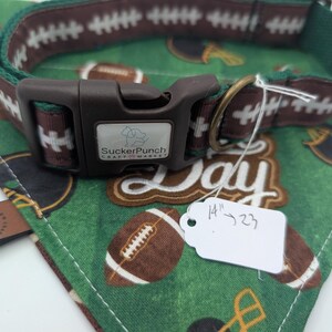 May include: A dog collar and bandana set with a football theme. The collar is brown with white football stitching and a dark green trim. The bandana is green with football and helmet graphics. The collar size is 14" to 23".