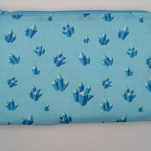 May include: A rectangular, light blue zippered pouch with a repeating pattern of stylized blue and white crystals. The zipper and stitching are also light blue. The pouch is likely made of fabric.