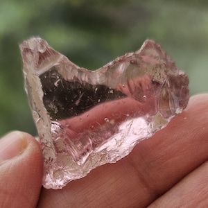 Puede incluir: Un trozo de vidrio de mar transparente, rosa y ligeramente iridiscente con una forma irregular y rugosa.