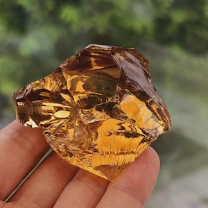 Puede incluir: Un gran cristal transparente de color ámbar con muchas facetas. El cristal está siendo sostenido en una mano.