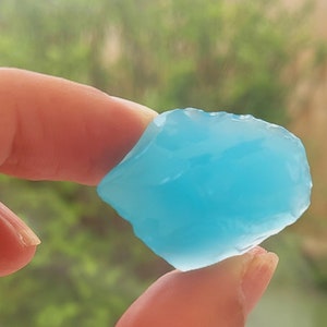 Puede incluir: Una mano sosteniendo un trozo de vidrio translúcido azul claro de forma irregular.