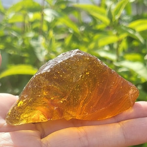 Puede incluir: Una gran pieza de vidrio de mar translúcido de color ámbar con una superficie lisa y redondeada. El vidrio tiene un ligero tono amarillo y es ligeramente iridiscente.