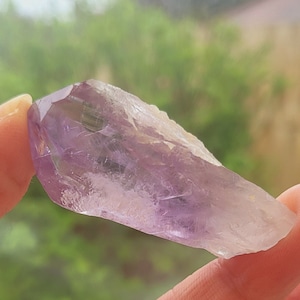 May include: A light purple amethyst crystal point with a smooth, polished surface. The crystal is translucent and has a slight shimmer.