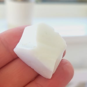 Puede incluir: Primer plano de una pieza blanca de carne de coco de forma irregular que se sostiene en una mano.