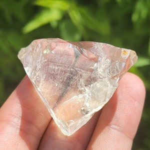 Puede incluir: Un cristal transparente y facetado con un tono ligeramente amarillo. El cristal tiene forma de diamante y tiene una textura rugosa y natural.
