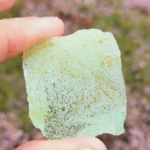 May include: A piece of sea glass with a light green color and a textured surface. The glass has small air bubbles trapped inside.