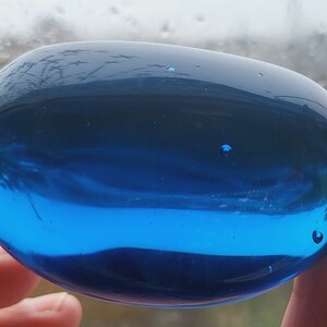 Puede incluir: Un pisapapeles de vidrio azul grande y liso. El vidrio es transparente y refleja la luz.