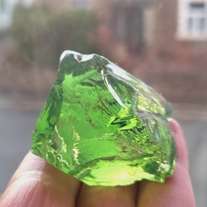 May include: A large, green, glass rock with a rough, irregular shape. The rock is translucent and has a slightly iridescent sheen.