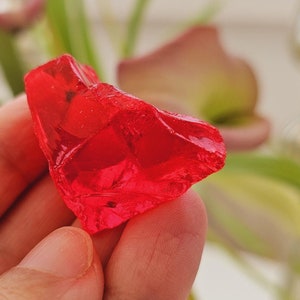 Könnte beinhalten: Ein leuchtend roter, durchsichtiger Glassplitter mit einer rauen, unregelmäßigen Form.