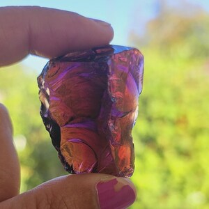 Puede incluir: Un gran cristal de amatista de forma irregular, de color morado oscuro con un ligero tono rojizo. El cristal es translúcido y tiene una superficie lisa y pulida.