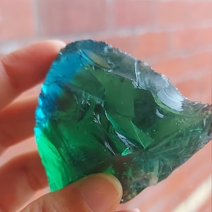 Puede incluir: Un gran fragmento de vidrio verde y azul con una forma irregular y rugosa.